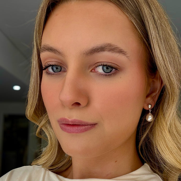 Close-up of a woman with blonde hair and blue eyes wearing pearl earrings.