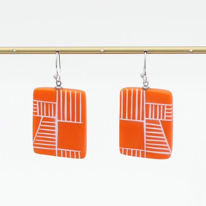 Orange earrings with white geometric pattern on a white background