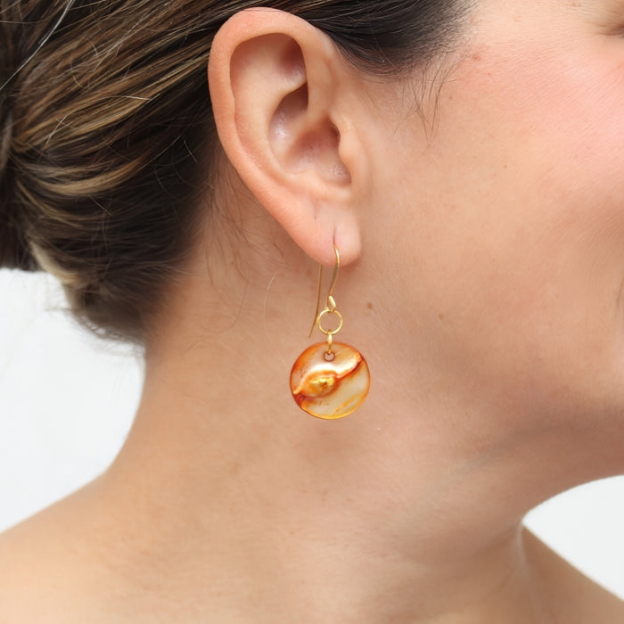 Close-up of an ear wearing a gold earring with a marbled design.