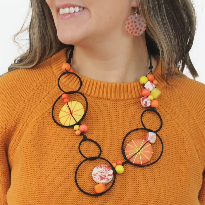 Person wearing a colorful necklace with circular and spherical beads on an orange sweater.