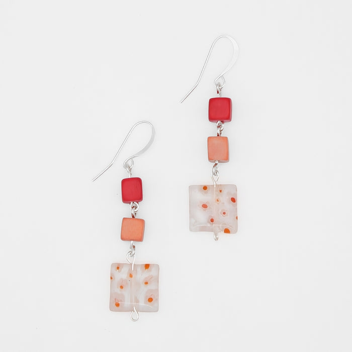 A pair of handmade dangle earrings featuring square glass beads in vibrant red, soft orange, and a milky white with orange speckles, suspended from silver fishhook wires on a clean white background.