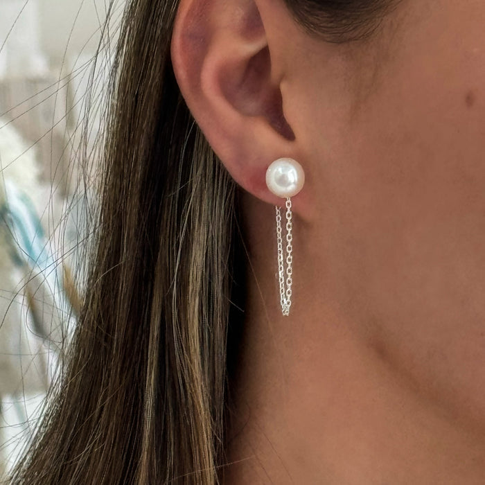 A close-up image of a woman's ear wearing a silver earring with a white pearl drop.