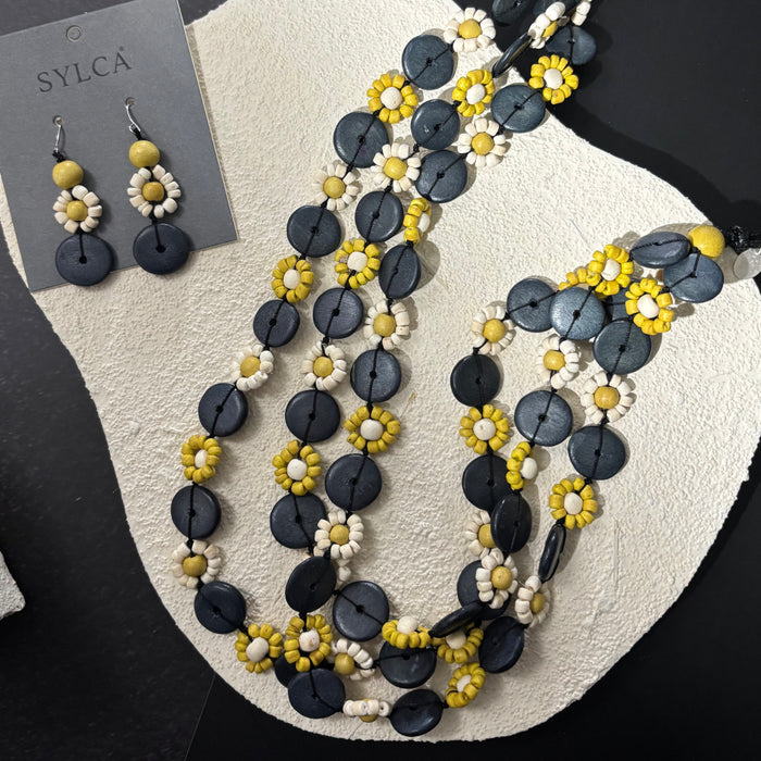 Necklace and earrings with black, yellow, and white beads on a textured surface.
