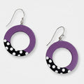 A pair of RESIN hoop earrings with a purple top half and a black bottom half decorated with white polka dots, hanging from silver fishhook wires on a light gray background.