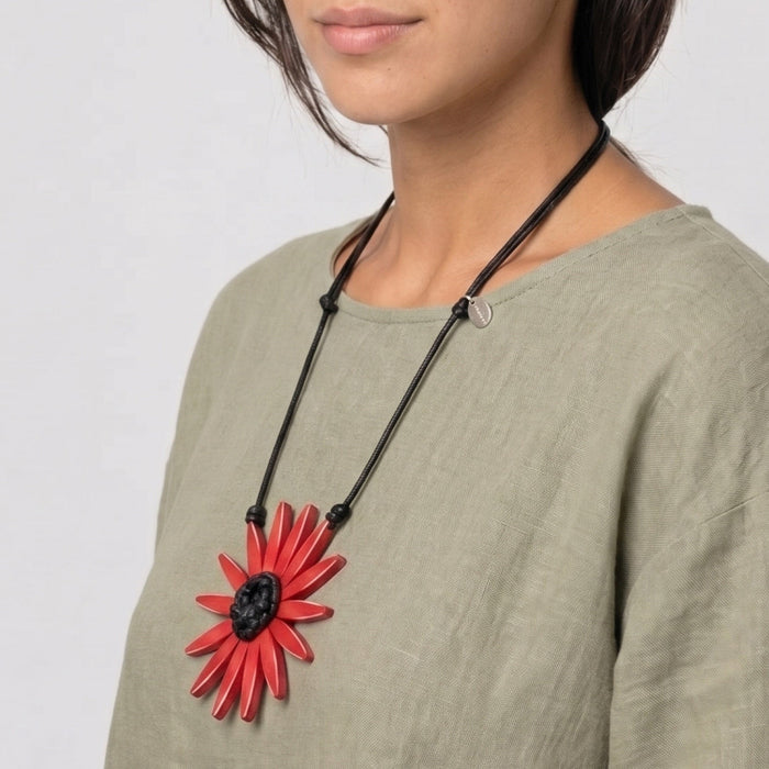 Woman wearing a necklace with a red flower pendant on a plain background