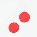 A pair of dangle earrings featuring round, matte red discs suspended from thin silver fishhook wires, set against a clean white background.