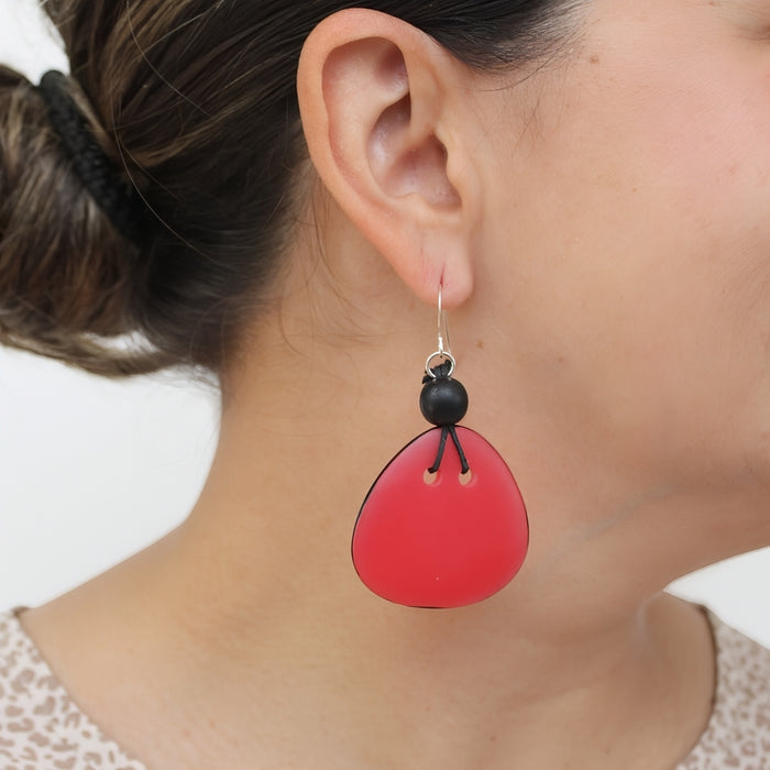 A close-up of a person's ear wearing a dangling earring with a bright red teardrop-shaped drop and a small black bead accent.