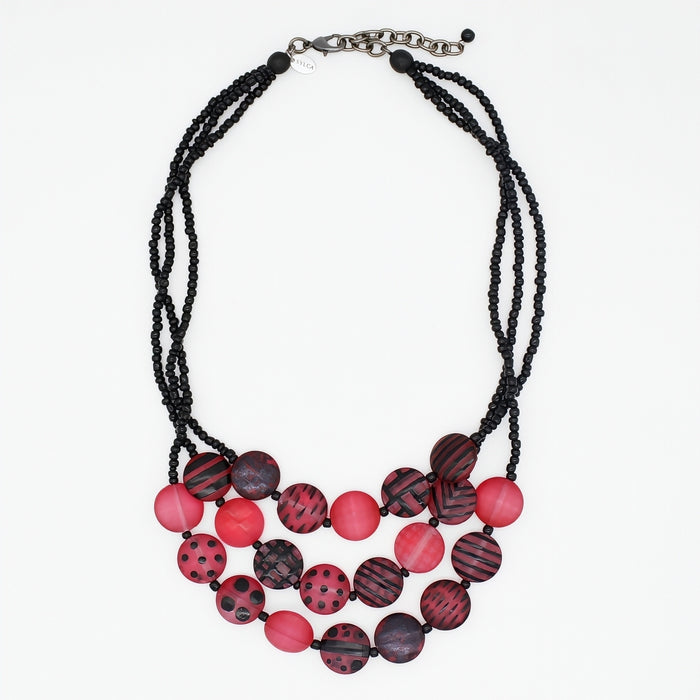 A multi-strand statement necklace featuring black beaded cords and round beads in shades of red, and black patterns, finished with a silver-tone clasp.
