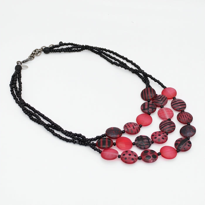 A multi-strand necklace featuring black beaded chains and a series of round, patterned beads in red, displayed on a clean white background.
