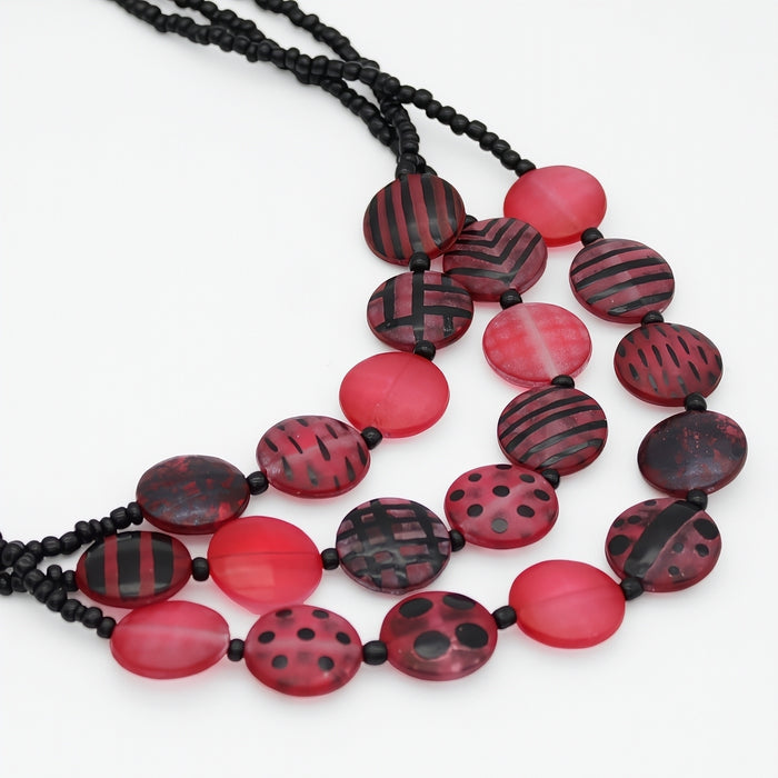 A multi-strand statement necklace featuring red and black patterned oval beads on a white background.