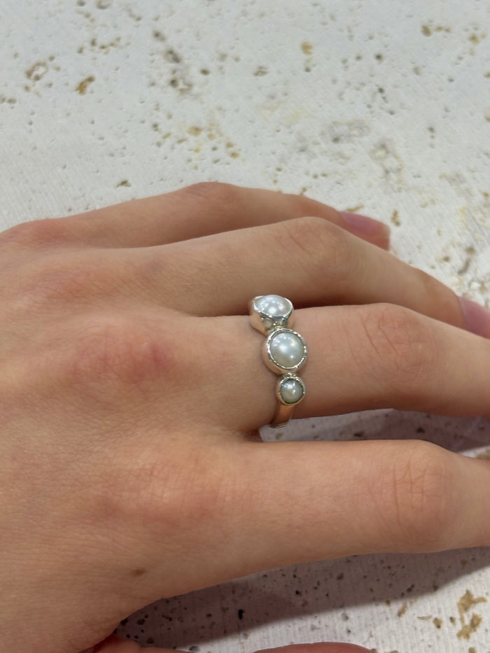 Hand wearing a silver ring with three pearls on a textured surface