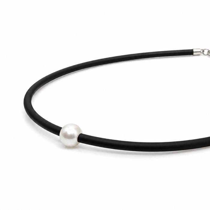 A minimalist black neoprene necklace featuring a single white pearl bead and a silver lobster clasp.
