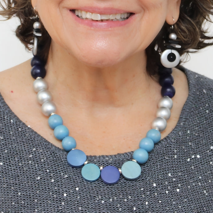 Close-up of a person wearing a blue and silver beaded necklace with earrings.