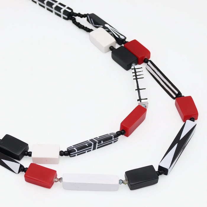 A modern geometric beaded necklace featuring red, black, white, and black-and-white patterned beads on a clean white background.
