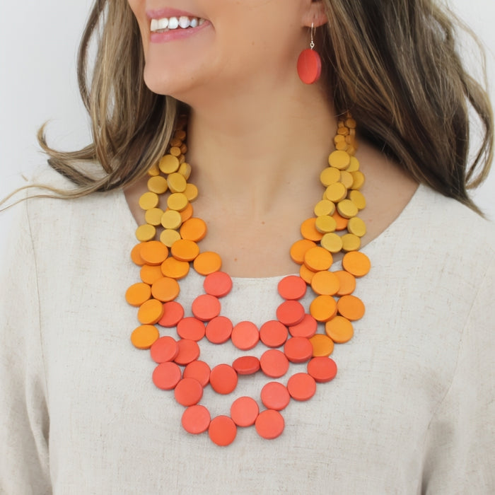 Woman wearing a orange and yellow colorful necklace with a plain background