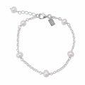 A silver chain bracelet with six white freshwater pearls spaced evenly along the chain, featuring a lobster clasp, extender chain, and a small engraved brand tag that reads 'LUSH'.