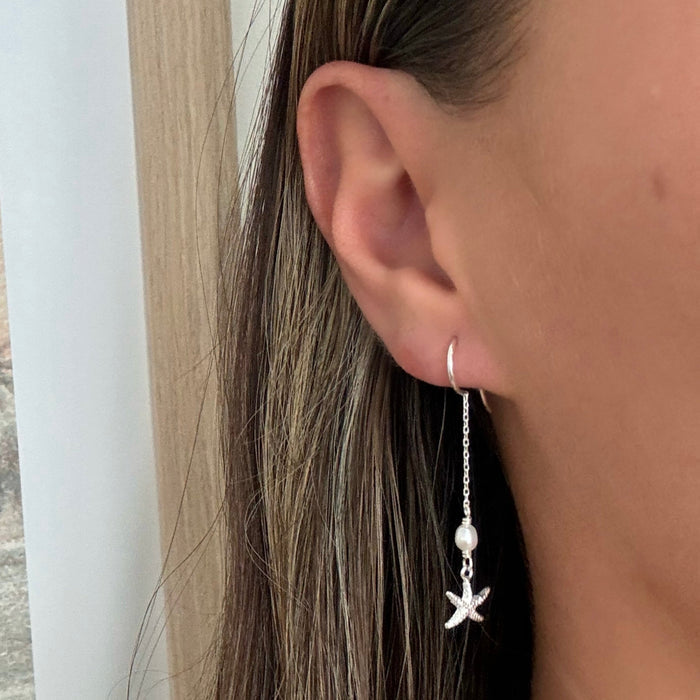 silver earring with a starfish design and pearls, dangling from a small hoop.