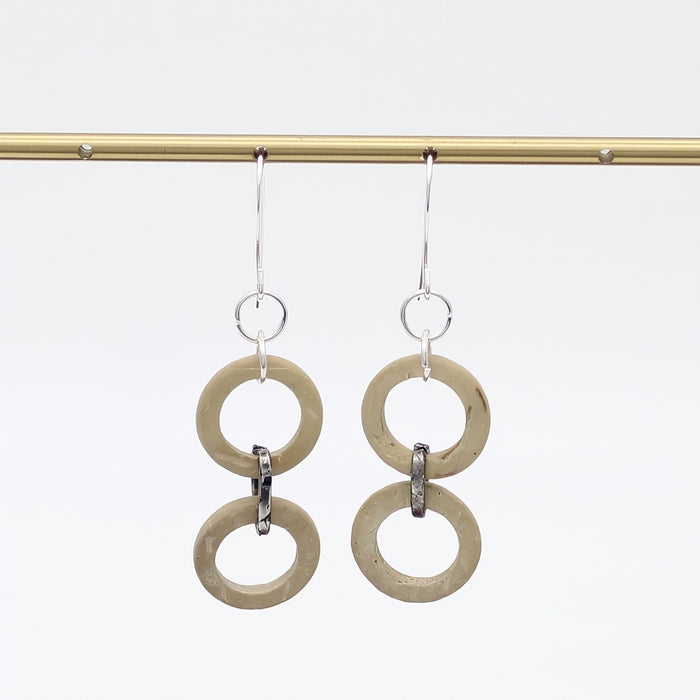Pair of earrings with circular designs hanging on a rod against a white background