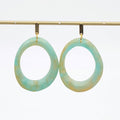 A pair of large, irregularly shaped hoop earrings with a marbled light blue and beige pattern, hanging from gold-toned hooks on a gold display bar against a white background.