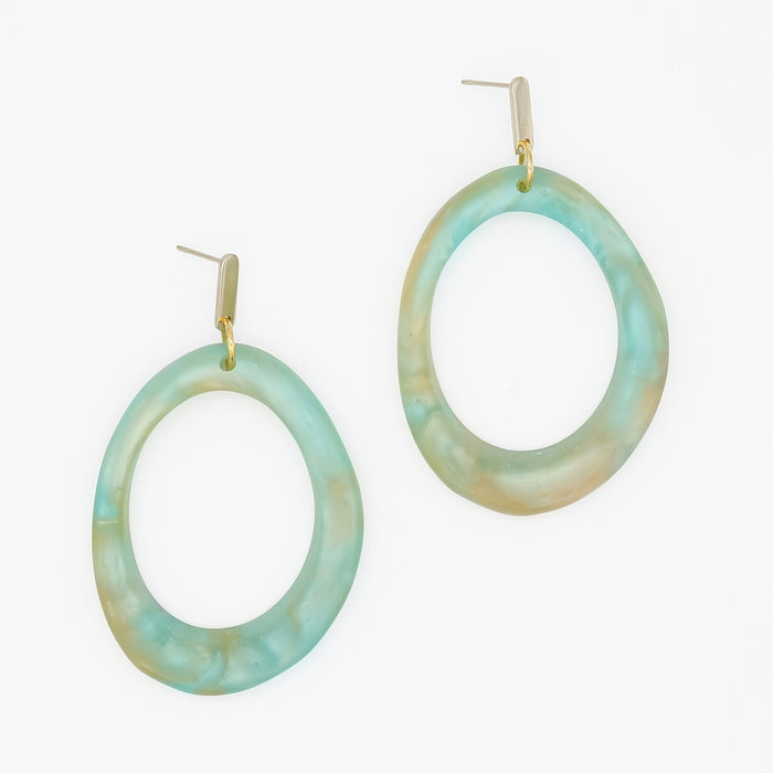 A pair of large, irregularly shaped oval drop earrings made of marbled light blue and beige resin, hanging from gold-tone posts on a plain white background.