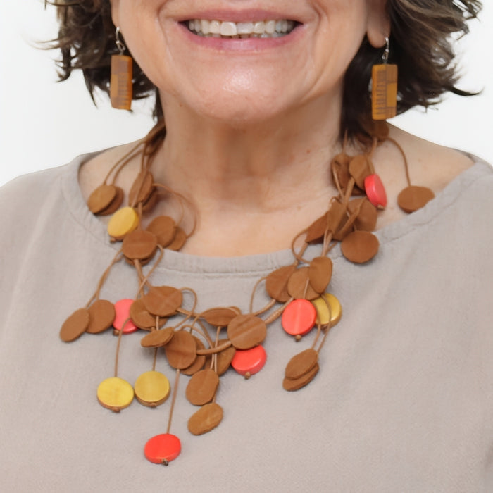Woman wearing a colorful necklace with wooden and multicolored circular pendants on a plain background