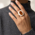 Close-up of a hand wearing a ring with a wooden center, against a neutral background.