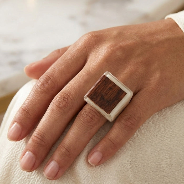 Hand wearing a ring with a wooden inlay on a light background