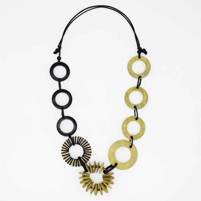 A modern statement necklace featuring alternating matte black circular discs and textured gold-tone disc and sunburst elements, suspended on a black cord against a plain white background.