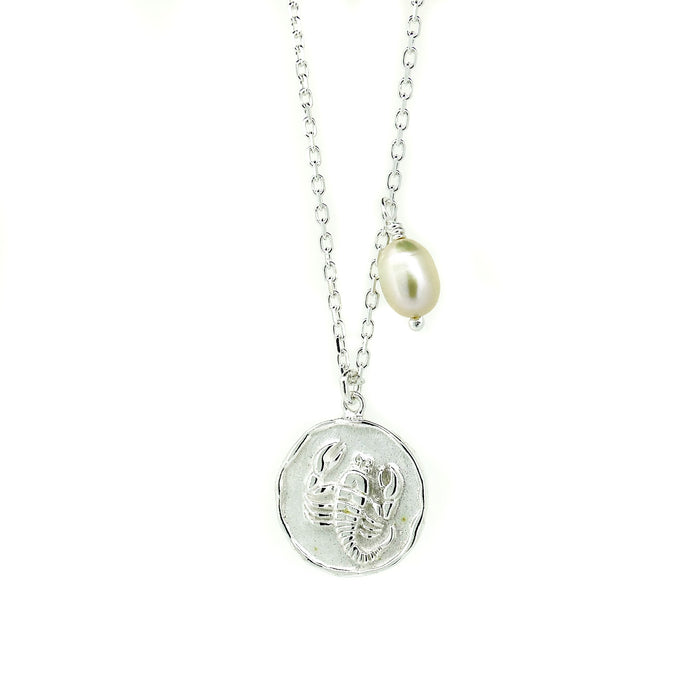 A silver necklace with a round pendant featuring the Scorpio zodiac symbol and a freshwater pearl charm attached to the chain.
