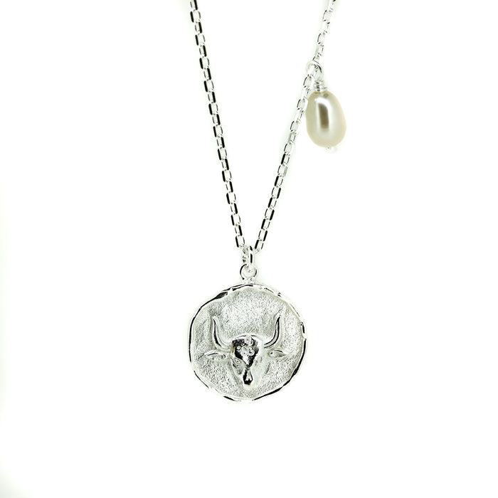 A silver necklace featuring a Taurus bull pendant with a lustrous pearl attached to the top.