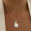 A silver necklace featuring a Pisces zodiac charm and a pearl, displayed on a person's neck.